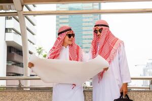 Arab Middle Eastern Businessman team with drawing paper blurry city background. Muslim engineer man checking project at building site photo