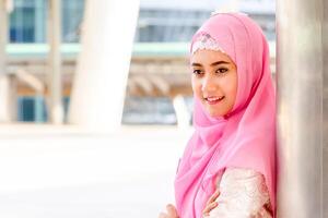 Portrait of a smiling young Arab Middle Eastern woman in the city blurred background, Muslim woman standing with arms crossed photo