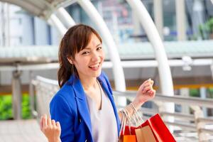 Cheerful young Asian woman carrying shopping bags while walking along the street. Shopping concepts photo