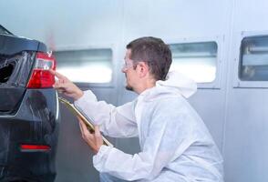 Worker man holding clipboard checklist of the car at the garage, Mechanic painting car in the chamber. Garage painting car service repair and maintenance photo