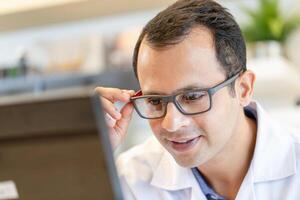 alegre optometrista hombre participación los anteojos en óptica almacenar, indio hombre elegir lentes a óptica tienda foto