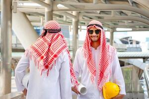 Arab Middle Eastern Businessman team with drawing paper blurry city background. Muslim engineer man checking project at building site photo