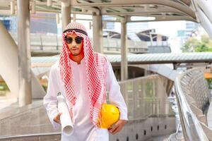 Arab Middle Eastern businessman with a blueprint blurry city background. Muslim engineer man checking project at building site photo