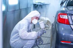 Mechanic painting car in chamber. Worker using spray gun and airbrush and painting a car, Garage painting car service repair and maintenance photo