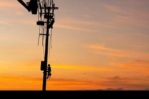 Silhouette of Electrician officer climbs a pole and uses a cable car to maintain a high voltage line system, Shadow of Electrician lineman repairman worker at climbing work on electric post power pole photo