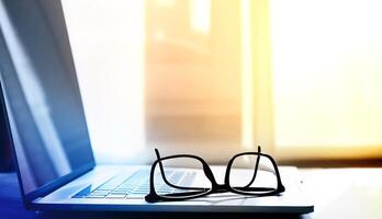 open laptop on which lie reading glasses in black frames. selective focus photo