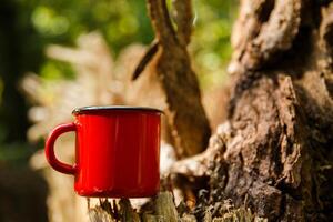 a red metal mug stands on a stump in a forest or park in the shade of trees on a sunny day. High quality photo