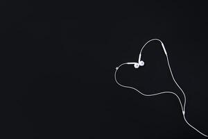 white headphones lie on a black background in the shape of a heart. Top view with copy space for text input. accessories. High quality photo