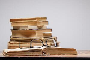 a stack of old books with bookmarks on a wooden table on a gray background. glasses lie on an open book. photo