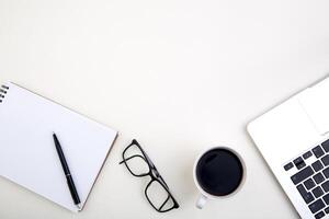 light office desk with laptop, white notebook mockup, glasses and coffee cup. Top view with copy space for text input. photo