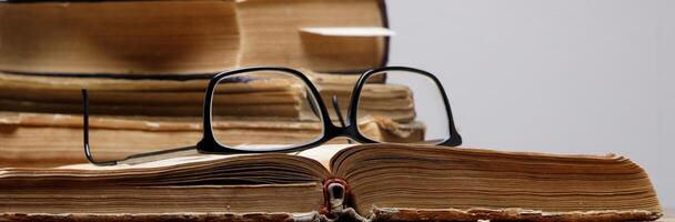 a stack of old books with bookmarks on a wooden table on a gray background. glasses lie on an open book.selective focus photo