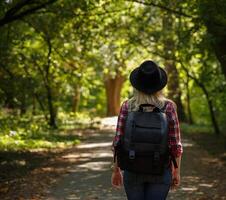 joven caucásico niña viajes en un sombrero y con un mochila mediante el bosque o parque en el sombra de arboles .fondo borroso. alto calidad foto