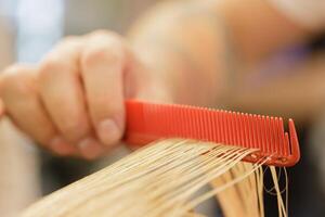 Stylist's hand holds a comb on which the model's blonde strand of hair. selective focus photo