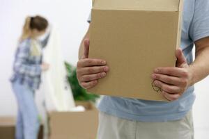 Close-up of a man with cardboard boxes moving into a new house. in the background a girl unpacks things. out of focus. High quality photo