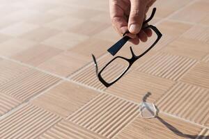 the hand of an unknown person picks up a broken spectacle frame on the street from a tile. High quality photo