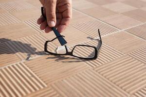 the hand of an unknown person picks up a broken spectacle frame on the street from a tile. High quality photo