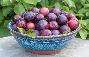 AI generated many plums in a blue bowl on a table full of leaves photo