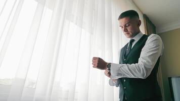 novio preparando para boda, hombre en formal atuendo comprobación su reloj de pulsera adentro, anticipación concepto. video