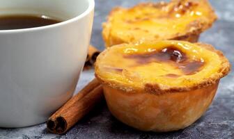 Lots of desserts Pastel de nata or Portuguese egg tart and cinnamon sticks with a cup of coffee. Pastel de Belm is a small pie with a crispy puff pastry crust and a custard cream filling. photo