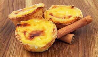 Three Pastel de nata or Portuguese egg tart and cinnamon sticks on a wooden brown background. Pastel de Belem is a small dessert, a cup-shaped pastry made from puff pastry with custard. photo