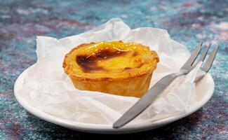 Plate with one Portuguese Pastel de Nata quiche. Pastel de Belem is a monastic and cult pastry in the form of cups with a burnt top and a crispy puff pastry crust. Sweet dessert with egg cream. photo