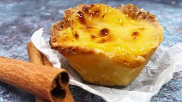 One Pastel de nata or Portuguese egg tart and cinnamon sticks. Pastel de Belm is a small pie with a crispy puff pastry crust and a custard cream filling. photo