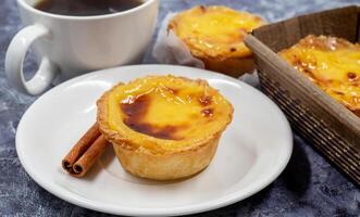 Lots of desserts Pastel de nata or Portuguese egg tart and cinnamon sticks with a cup of coffee. Pastel de Belm is a small pie with a crispy puff pastry crust and a custard cream filling. photo