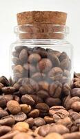 Coffee beans in a small glass jar with a cork lid on the table. Coffee beans packed in a transparent, airtight storage container. Coffee seeds inside a glass jar. photo