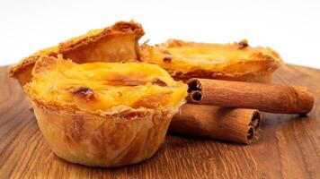 Three Pastel de nata or Portuguese egg tart and cinnamon sticks on a wooden brown background. Pastel de Belem is a small dessert, a cup-shaped pastry made from puff pastry with custard. photo