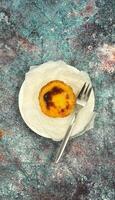 One Pastel de nata or Portuguese egg tart on a white plate. Pastel de Belm is a small pie with a crispy puff pastry crust and a custard cream filling. photo