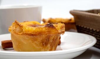 One Pastel de nata or Portuguese egg tart on a white plate. Pastel de Belm is a small pie with a crispy puff pastry crust and a custard cream filling. photo