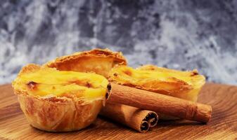 Pastel de nata tarts or Portuguese egg tart and cinnamon sticks on a wooden brown background. Pastel de Belem is a small pie with a crispy puff pastry crust and a custard cream filling. photo