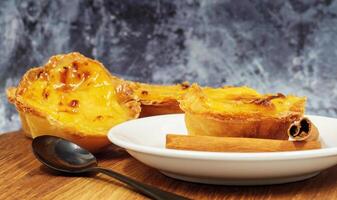 Pastel de nata tarts or Portuguese egg tart and cinnamon sticks on a wooden brown background. Pastel de Belem is a small pie with a crispy puff pastry crust and a custard cream filling. photo