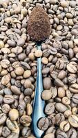 Against the background of roasted aromatic coffee beans lies a metal spoon filled with ground coffee. A drink made from roasted and ground beans from the coffee tree or coffee bush. photo