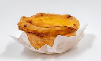 One Portuguese Pastel de Nata pie with custard and cinnamon sticks on a white plate. Pastel de Belem is an iconic cup-shaped pastry with a burnt top and a crispy puff pastry crust. Sweet dessert. photo