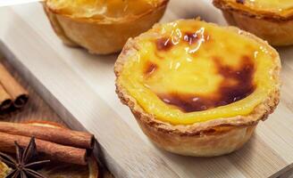 Three Pastel de nata or Portuguese egg tart and cinnamon sticks on a wooden brown background. Pastel de Belem is a small dessert, a cup-shaped pastry made from puff pastry with custard. photo