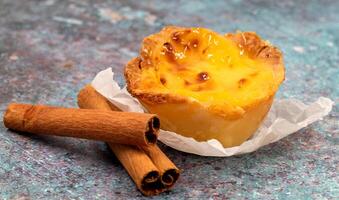 One Pastel de nata or Portuguese egg tart and cinnamon sticks. Pastel de Belm is a small pie with a crispy puff pastry crust and a custard cream filling. photo