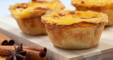 Pastel de nata tarts or Portuguese egg tart and cinnamon sticks on a wooden brown background. Pastel de Belem is a small pie with a crispy puff pastry crust and a custard cream filling. photo