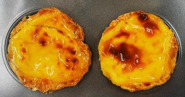 Two freshly baked Pastel de nata or Portuguese egg tart desserts in a baking dish. Pastel de Belm is a small pie with a crispy puff pastry crust and a custard cream filling. photo
