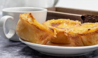 Lots of desserts Pastel de nata or Portuguese egg tart with a white cup of black coffee. Pastel de Belm is a small pie with a crispy puff pastry crust and a custard cream filling. photo