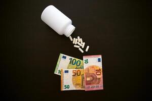 Jar with tablets medicinal capsules on a black table 10 5 euros paper banknotes photo