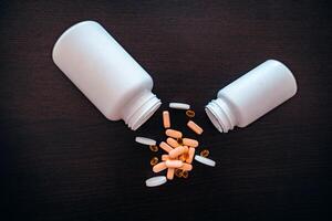 Two white jars with scattered red, pink and black medicines on a dark table. photo