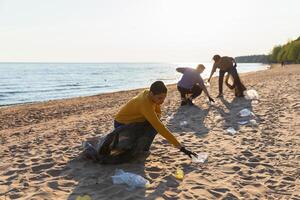 tierra día. voluntarios activistas recoge basura limpieza de playa costero zona. mujer y mans pone el plastico basura en basura bolso en Oceano costa. ambiental conservación costero zona limpieza foto