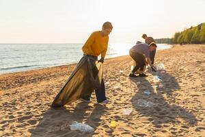 tierra día. voluntarios activistas recoge basura limpieza de playa costero zona. mujer y mans pone el plastico basura en basura bolso en Oceano costa. ambiental conservación costero zona limpieza foto