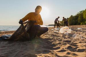 tierra día. voluntarios activistas recoge basura limpieza de playa costero zona. mujer y mans pone el plastico basura en basura bolso en Oceano costa. ambiental conservación costero zona limpieza foto