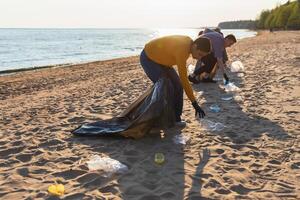 tierra día. voluntarios activistas recoge basura limpieza de playa costero zona. mujer y mans pone el plastico basura en basura bolso en Oceano costa. ambiental conservación costero zona limpieza foto