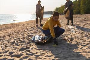 Earth day. Volunteers activists collects garbage cleaning of beach coastal zone. Woman and mans puts plastic trash in garbage bag on ocean shore. Environmental conservation coastal zone cleaning photo