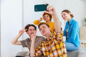 Cheers Funky mood. Happy group of friends make selfie. Man taking photo of friends at party. Group of multiracial young people taking photo on phone. Young people enjoy their company smile have fun