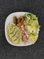 hecho en casa A la parrilla pollo con calabacín guiso, verde ensalada y Pepino pepinillos servido en un blanco plato foto