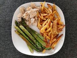 hecho en casa A la parrilla pollo con francés papas fritas y A la parrilla espárragos, servido en un blanco plato foto